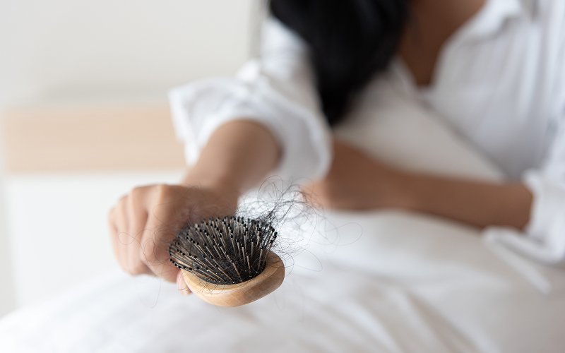 Woman-holding-hairbrush-showing-postpartum-hair-loss-problem